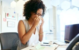 Young woman sat at her desk blowing her nose.