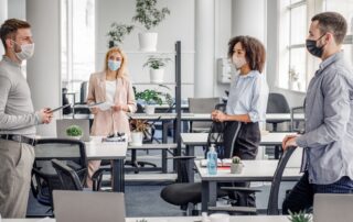 Multiracial colleagues in an office wearing protective face masks with a hand sanitiser on a nearby desk