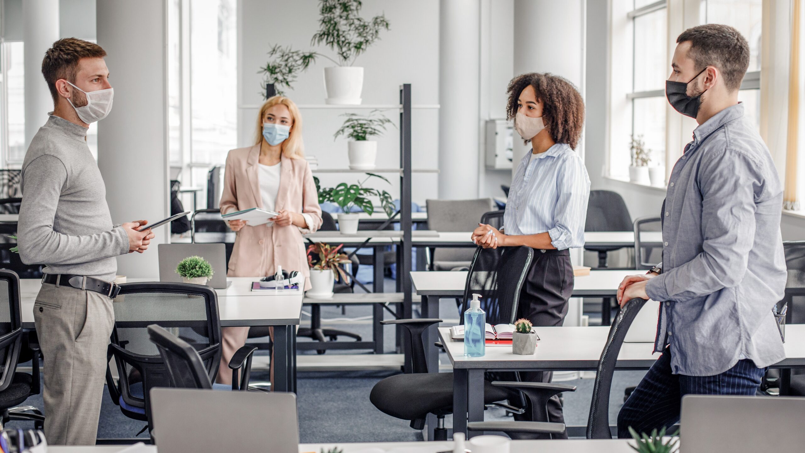 Multiracial colleagues in an office wearing protective face masks with a hand sanitiser on a nearby desk