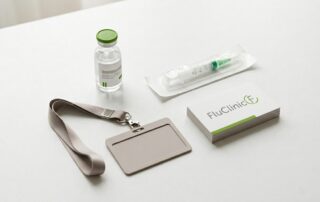 Flu vaccine vial and syringe arranged on a white surface with corporate ID lanyard, representing corporate flu vaccination services as an alternative to CityDoc